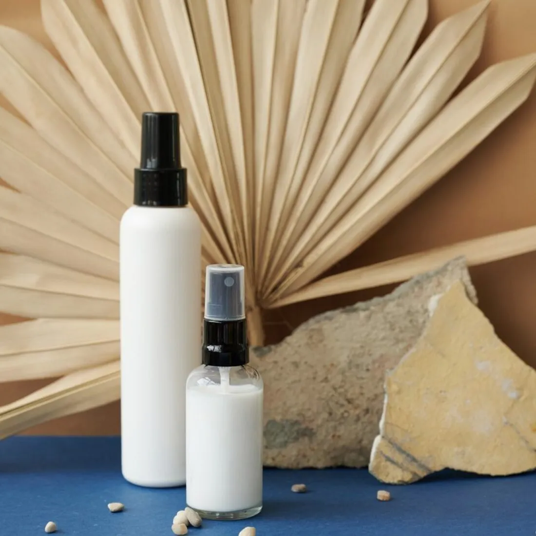Envases blancos de cosmética junto a una hoja de palma
