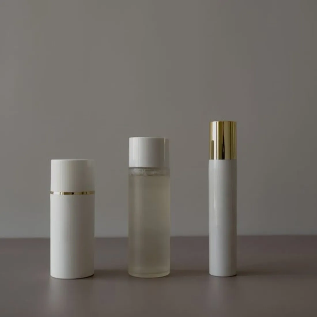 Tres envases de cosmética alineados sobre fondo gris claro